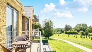A balcony with wicker furniture, a glass door, and a view of a green landscape. - Cotswolds Apartment 3 Sleeps 9 (Chipping Norton)