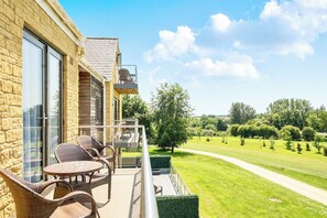 Ein Balkon mit Korbmöbeln, einer Glastür und Blick auf eine grüne Landschaft.