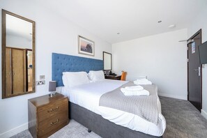 Ein Hotelzimmer mit einem großen Bett, einem Holzschrank, einem Schreibtisch mit Stuhl und einem durch eine Tür einsehbaren Badezimmer.