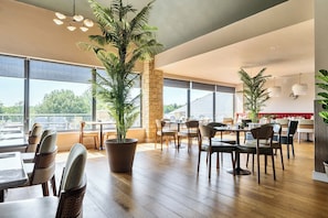 Un vaste espace dédié à la salle à manger, avec de hauts plafonds, de grandes fenêtres et des plantes en pot.