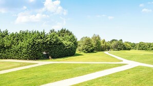 A well-maintained grassy area with a winding path and dense coniferous trees in the background. - Cotswolds Apartment 3 Sleeps 9 (Chipping Norton)