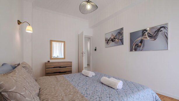 Une chambre à coucher comprenant un lit, une table de chevet, une commode et deux tableaux abstraits accrochés au mur.