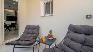 Un espace de vie moderne avec deux fauteuils gris confortables, une petite table sur laquelle se trouve un panier de fruits et des boissons, et une vue sur la salle à manger à travers une porte vitrée.