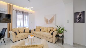 Un salon moderne avec un canapé d’angle beige, un téléviseur à écran plat, un luminaire suspendu au plafond et une plante en pot.