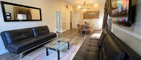 A living room with a black leather sofa, a glass coffee table, and a dining area with a table and chairs.