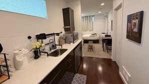 Quarto de hotel pequeno com cozinha compacta, cama, escrivaninha e banheiro.