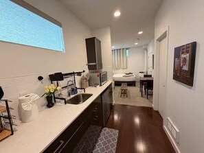 A compact hotel room with a kitchenette, a bed, a desk, and a bathroom. - The May Townhome - Lower (Seattle)