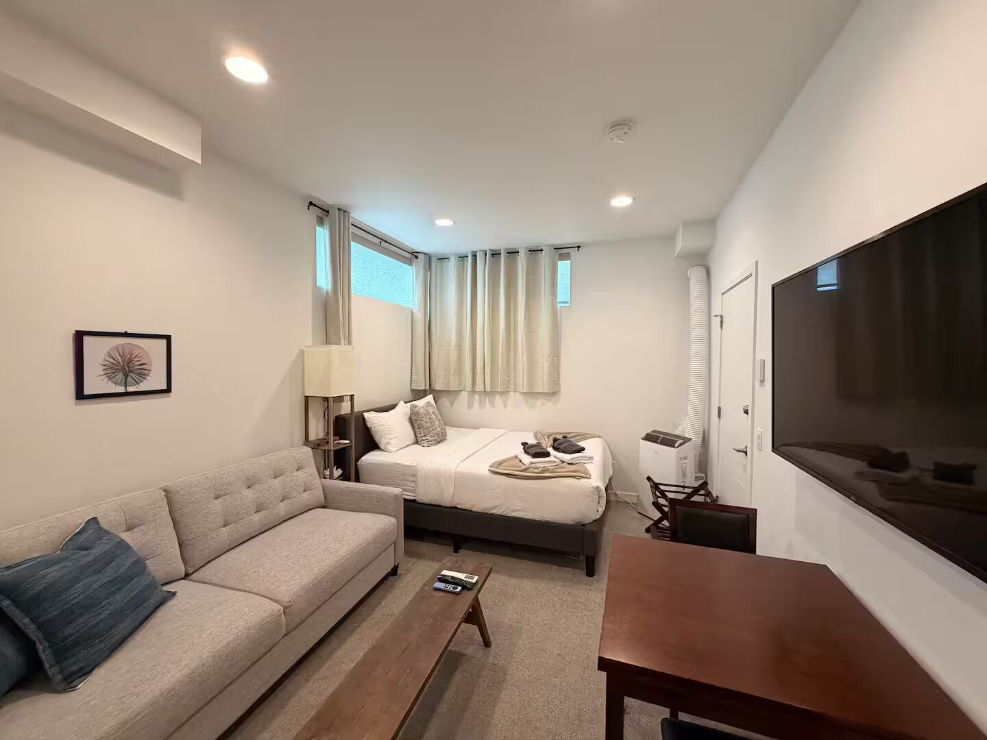 A modern hotel room with a sofa, a bed, a TV, and a lamp.