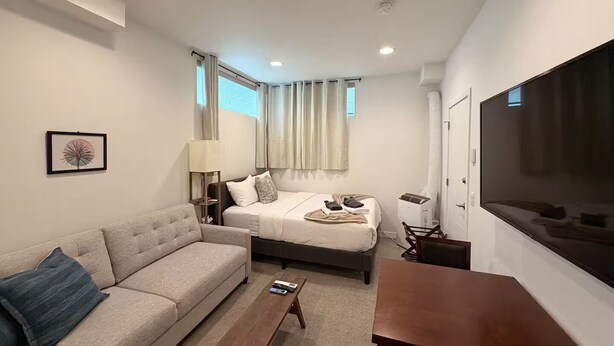 Quarto de hotel moderno com sofá, cama, televisão e luminária.
