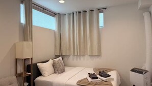 Um quarto com cama, mesa de cabeceira, luminária, janela com cortinas e ar condicionado.