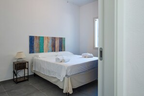 Ein Schlafzimmer mit einem Bett, einem Nachttisch, einer Lampe und einem farbenfrohen Kunstwerk an der Wand.