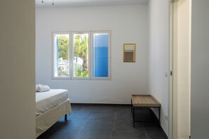 Un dormitorio con una cama, una mesita, una ventana con persianas y una puerta.