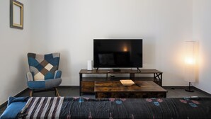 Ein Zimmer mit einem Bett, einem Fernseher auf einem Holzständer, einem Sessel und einer Lampe.