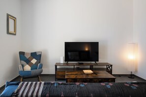 A room with a bed, a TV on a wooden stand, a chair, and a lamp. - Villa Sun and Moon by Ortigiaapartments (Plemmirio)