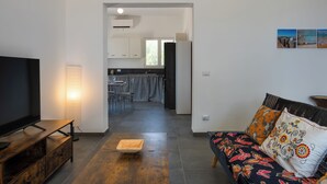 Ein modernes Wohnzimmer mit Flachbildfernseher, einer Couch mit gemusterten Kissen und einem Essbereich mit kariertem Tischlein.