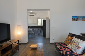 A modern living room with a flat-screen TV, a sofa with patterned cushions, and a dining area with a checkered tablecloth. - Villa Sun and Moon by Ortigiaapartments (Plemmirio)
