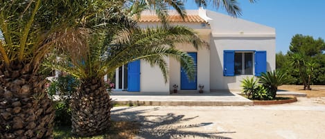 Un bâtiment blanc avec des volets bleus, un palmier au premier plan et un ciel dégagé.
