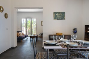 A dining area with a table set for four, a sofa in the background, and a large window with a view of palm trees. - Villa Sun and Moon by Ortigiaapartments (Plemmirio)