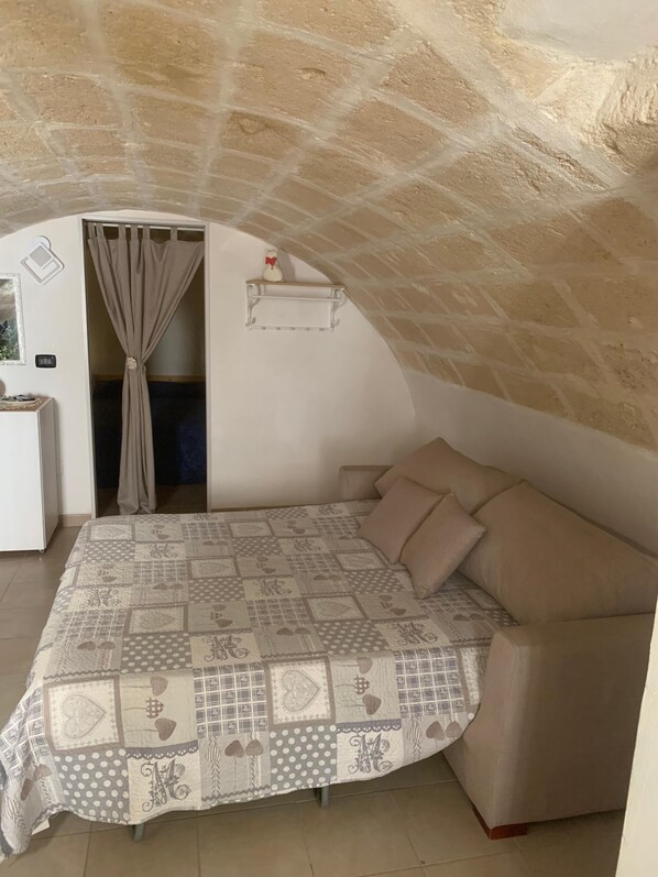 A bedroom with a bed, a sofa, a curtain, a shelf, and a stone ceiling.