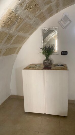 A room with a white cabinet, a mirror, a vase with flowers, and a tiled floor.