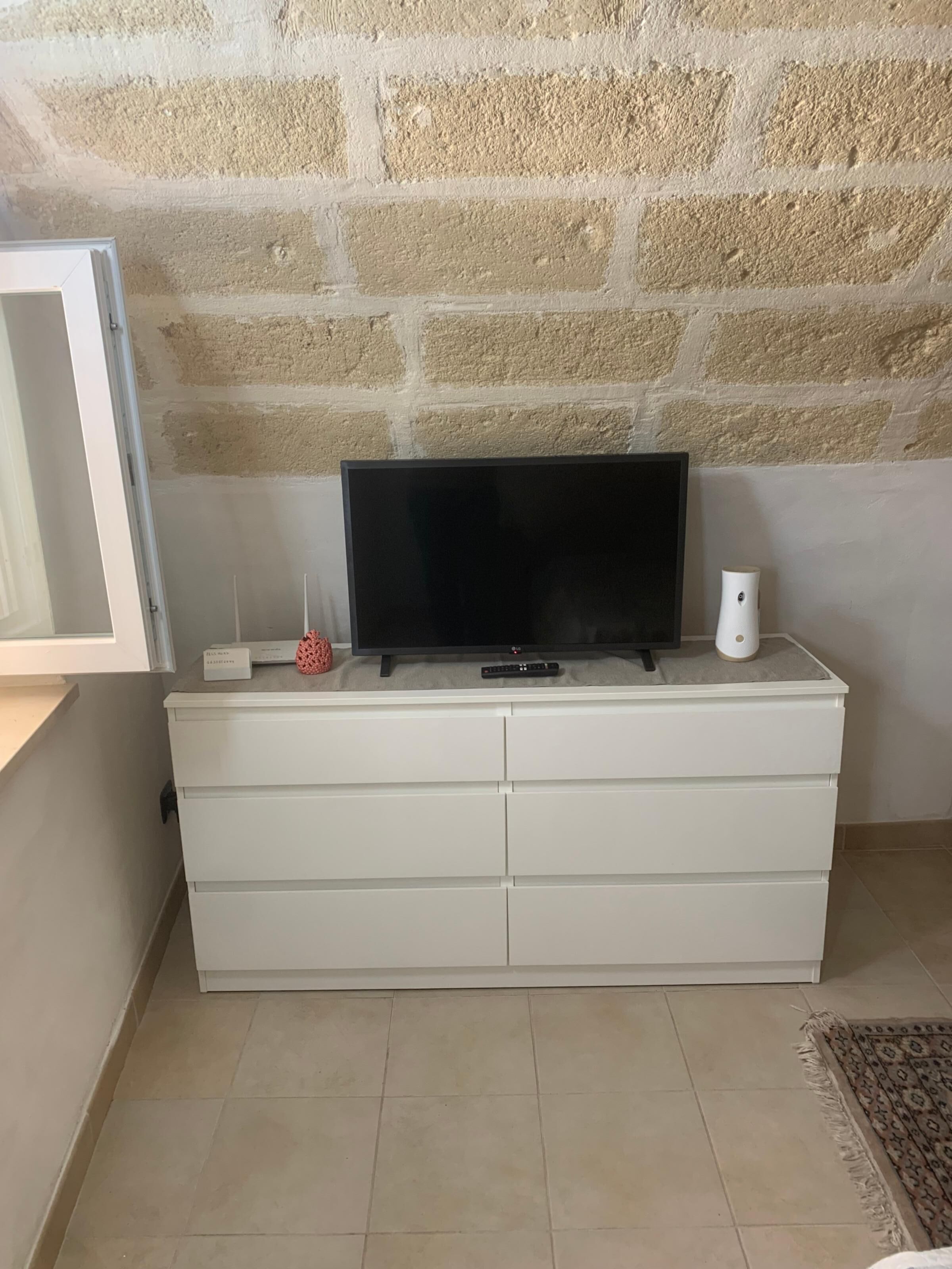 A white dresser with a flat-screen TV, a remote, and a small decorative item.