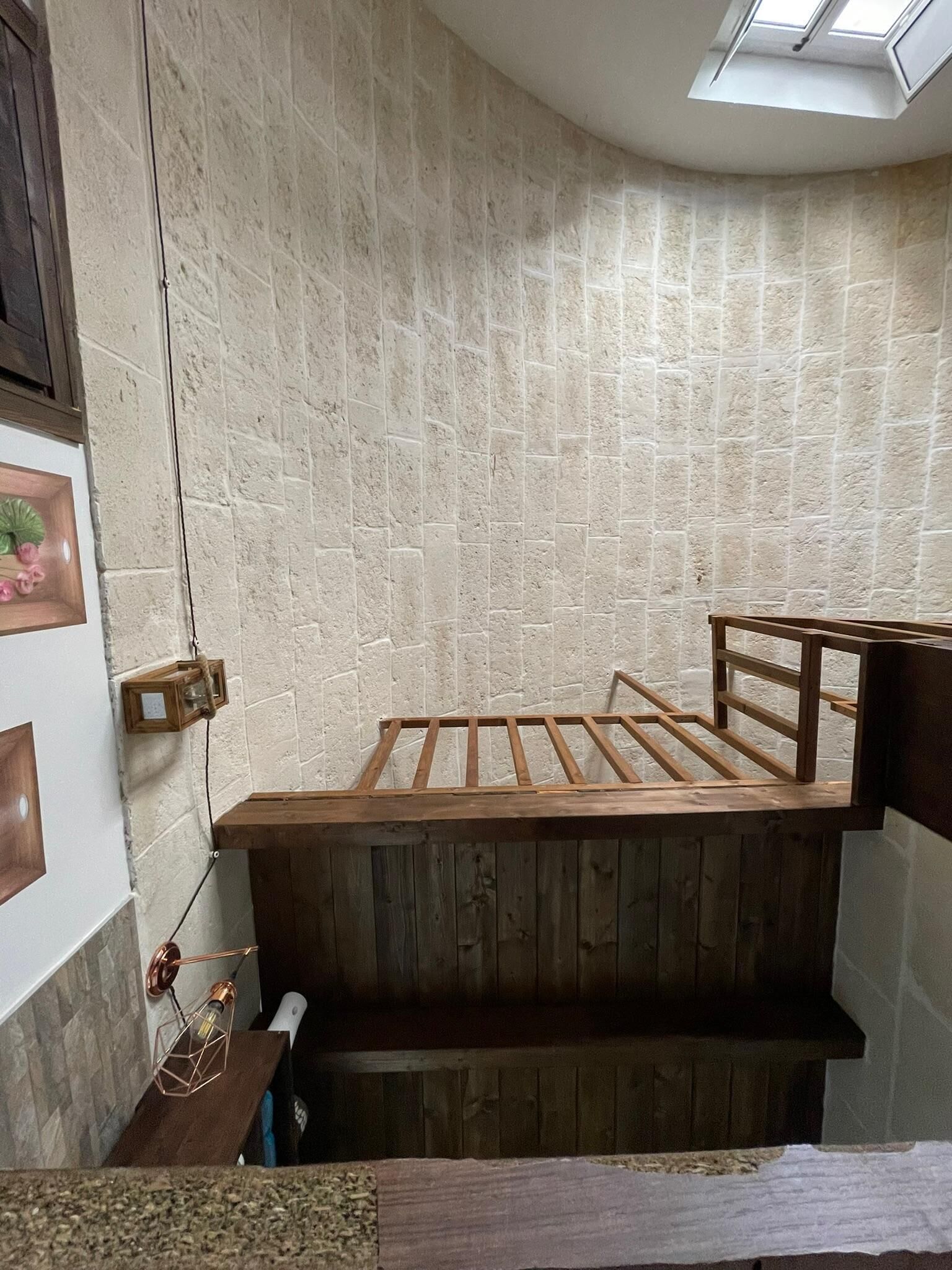 Une chambre d’angle avec un plafond en pente, un puits de lumière, un cadre de lit en bois et une petite étagère en bois.