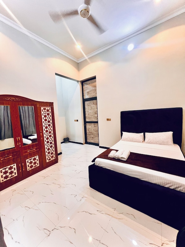 A hotel room with a bed, a wardrobe, a ceiling fan, and a door leading to another room.