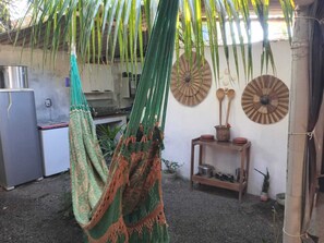 A hammock hanging under a palm tree, a rustic shelf with pots, and a metal water heater. - Casa rústica com todo charme do litoral (Maraú)
