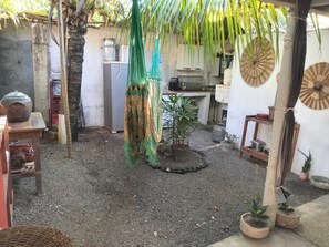 A courtyard with a rustic kitchen area, a hanging green cloth, and potted plants. - Casa rústica com todo charme do litoral (Maraú)