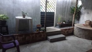 A small, enclosed outdoor area with a concrete floor, a wooden stool, a purple chair, and several potted plants. - Casa rústica com todo charme do litoral (Maraú)