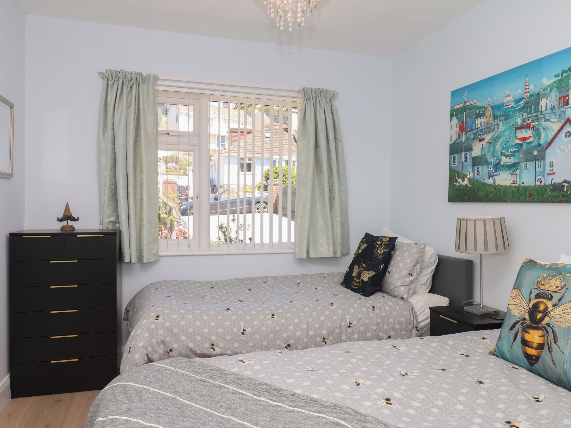 A bedroom with two beds, a dresser, a painting, and a window with curtains.