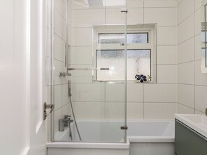 Ein modernes Badezimmer mit einer in Glas abgeschirmten Dusche, einer Badewanne und einem Fenster mit Milchglas.