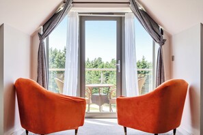 Quarto com duas cadeiras laranja voltadas para uma varanda com vista para o verde.