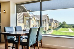 Uma área de refeições com mesa e cadeiras, amplas janelas e vista para uma fileira de casas urbanas.