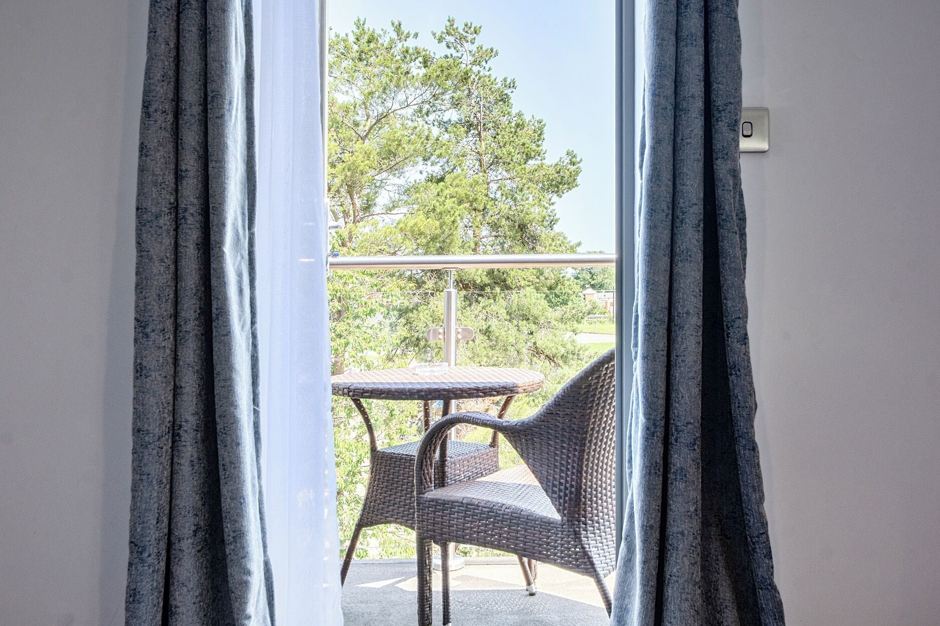 A balcony with wicker furniture, a metal railing, and a view of trees and a building.