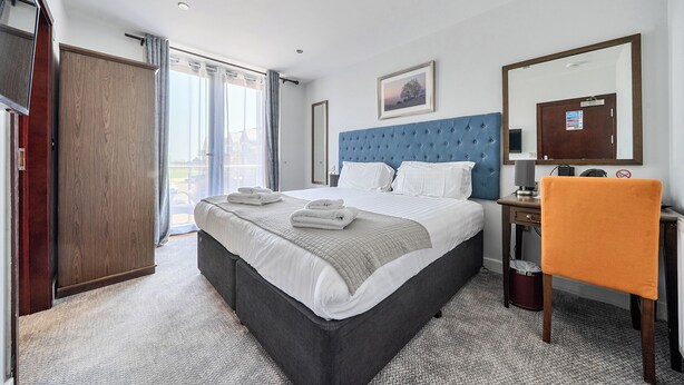 A hotel room with a large bed, a desk, a chair, a mirror, and a view of the outside. - Cotswolds Apartment 4, Sleeps 9 (Chipping Norton)