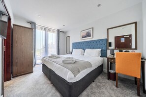Quarto de hotel com uma cama grande, uma escrivaninha, uma cadeira, um espelho e vista para o exterior.