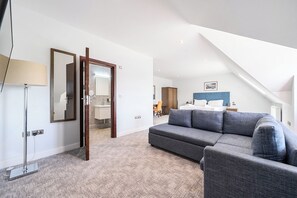 A modern bedroom with a large bed, a sofa, and a bathroom visible through an open door. - Cotswolds Apartment 4, Sleeps 9 (Chipping Norton)