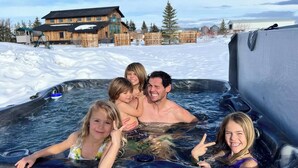 Eine Familie in einer Whirlpoolanlage, im Hintergrund eine Holzhütte.
