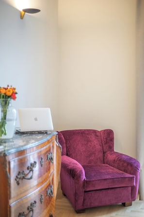 Ein Zimmer mit einem hölzernen Schminktisch, einem Laptop, einem rosa Sessel und einer Vase mit Blumen.