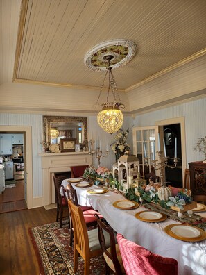Une salle à manger avec une longue table dressée pour six personnes, un lustre et un miroir au-dessus de la table.