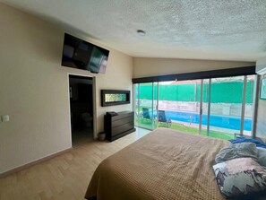 Ein Schlafzimmer mit einem großen Bett, einem an der Wand befestigten Fernseher und einer Glastür zu einem Poolbereich.