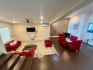 Uma sala de estar moderna com sofás vermelhos, uma mesa de centro de vidro e uma TV fixada na parede.