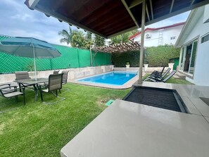 Ein Garten mit Swimmingpool, überdachter Terrasse und Rasen.