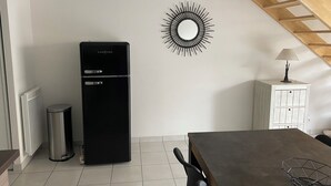 A modern kitchen with a black refrigerator, a trash bin, a dining table, and a wall-mounted mirror. - Joalland's Cozy Retreat, 50 meters from the beach (La Plaine-sur-Mer)