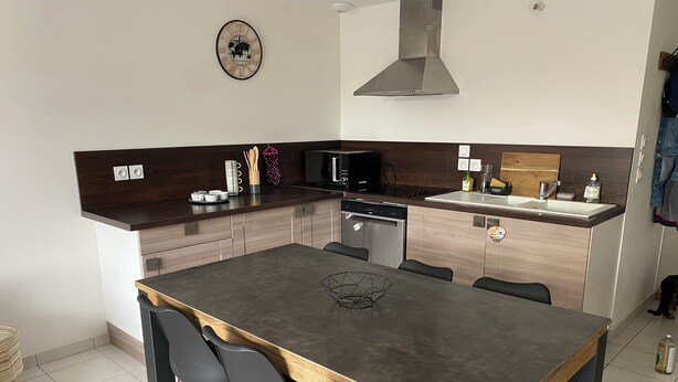 A modern kitchen with a central island, built-in appliances, and a dining area with chairs. - Joalland's Cozy Retreat, 50 meters from the beach (La Plaine-sur-Mer)