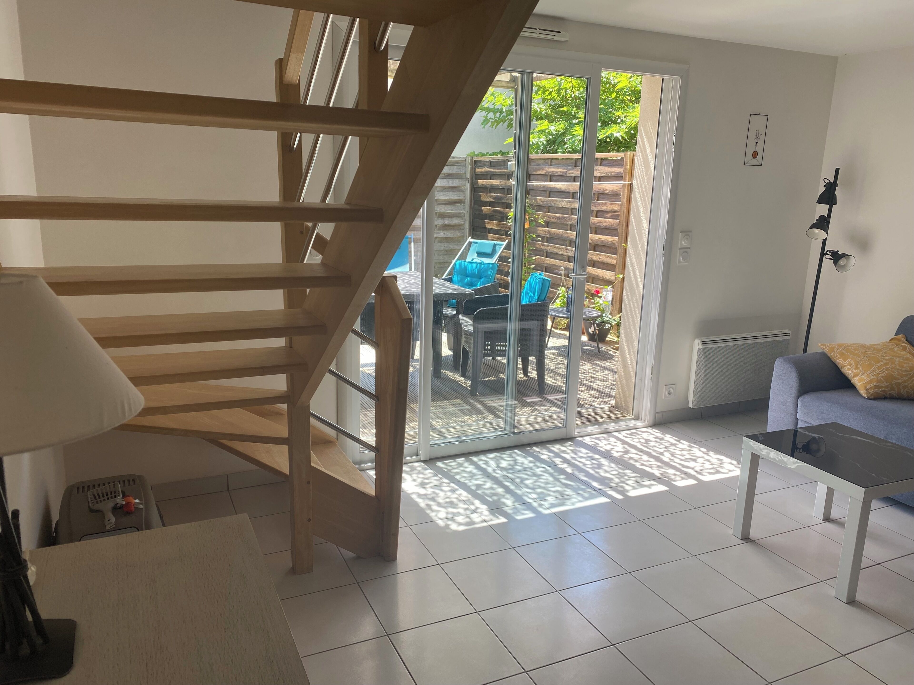 A modern interior with a wooden staircase, a sliding glass door leading to an outdoor patio, and a sofa with a patterned cushion.