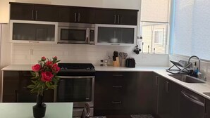 A modern kitchen with dark cabinets, stainless steel appliances, and a dining area with a vase of flowers. - The May Townhome - Upper (Seattle)
