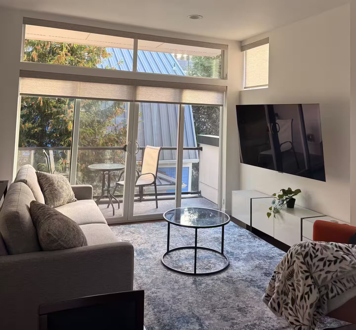 A modern living room with a sofa, a coffee table, a TV, and a balcony with a table and chairs.