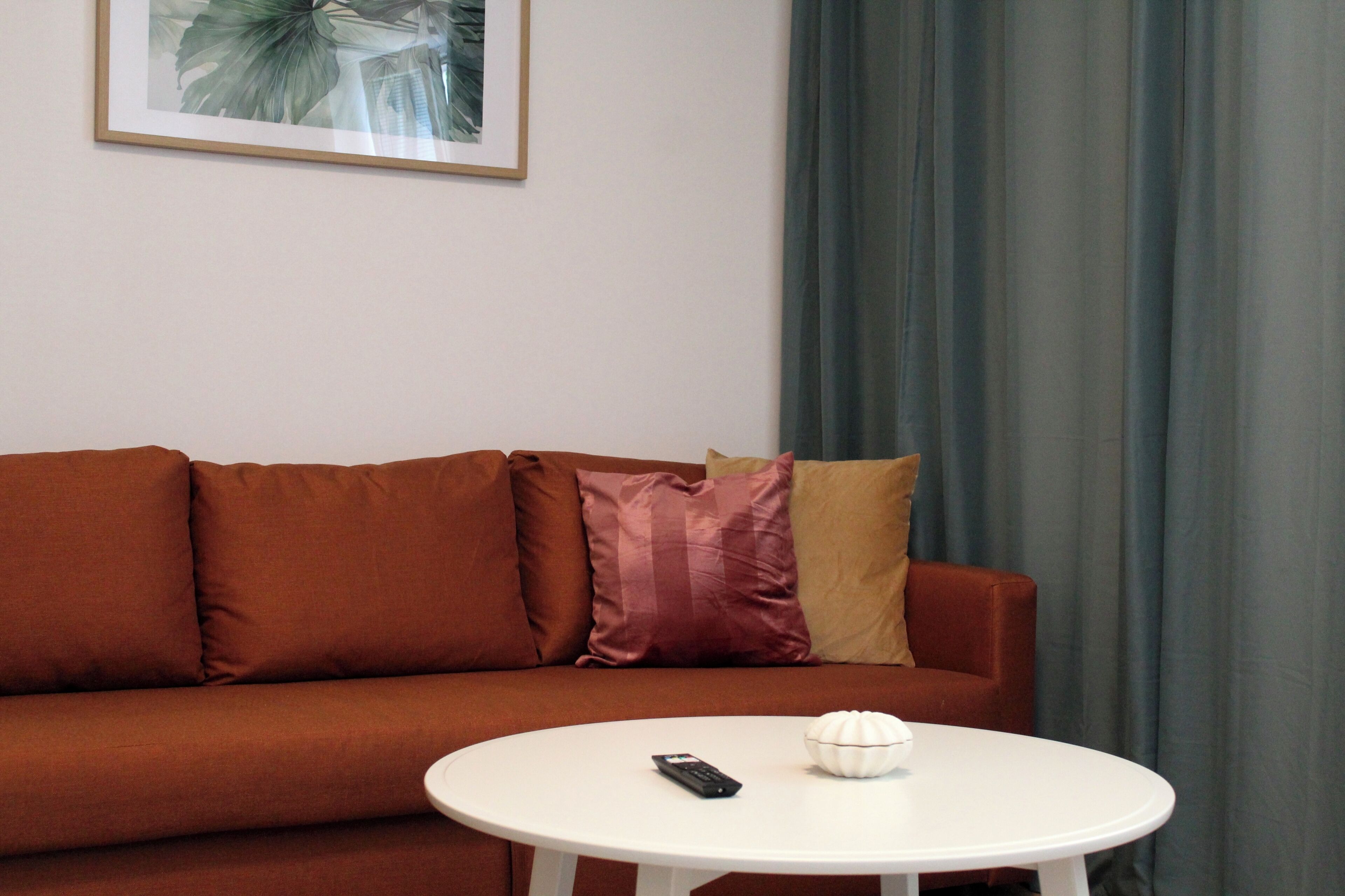Ein Zimmer mit einem braunen Sofa, einem weißen Tisch, einer Fernbedienung und einem weißen Dekorationsobjekt.